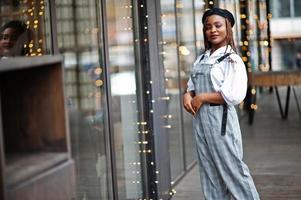 mulher afro-americana de macacão e boina posou no terraço ao ar livre com guirlanda de decorações de natal. foto