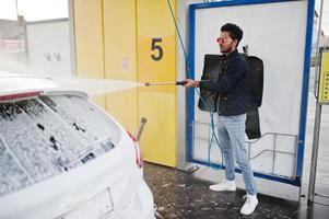 homem do sul da Ásia ou homem indiano lavando seu transporte branco na lavagem de carros. foto