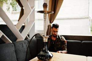 feche o cachimbo de água contra o homem árabe de barba elegante. foto