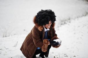 mulher afro-americana de cabelo encaracolado usa casaco de pele de carneiro e luvas posadas no dia de inverno. foto