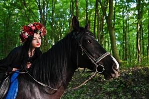 garota mística em grinalda veste de preto a cavalo em madeira. foto