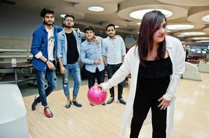 mulher do sul da Ásia em pé na pista de boliche com bola nas mãos. garota está se preparando para um lance. amigos a apoiam em voz alta. foto