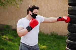 retrato esportivo homem boxer árabe em máscara facial médica preta boxe ao ar livre durante a quarentena de coronavírus. foto