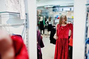 loira experimenta um vestido vermelho na boutique, olhando no espelho. foto