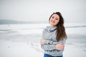 garota engraçada usar suéter com capuz e jeans, no lago congelado em dia de inverno. foto