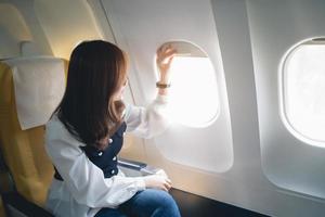 mulher asiática sentada em um assento no avião e olhando pela janela indo em uma viagem, passageira mulher asiática está saindo para uma viagem de avião de férias. conceito de viagens de férias. foto