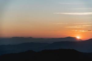 paisagem por do sol com iluminação de ouro de montanha e sol sob o céu de noite colorido vibrante nas montanhas. natureza montanha céu e nuvens conceito de pôr do sol foto