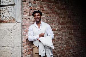 pensativo jovem cavalheiro afro-americano bonito em trajes formais. homem preto elegante modelo de casaco branco. foto