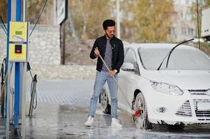 homem do sul da Ásia ou homem indiano lavando seu transporte branco na lavagem de carros. foto