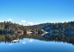 céu azul sobre floresta e lago com barco branco foto