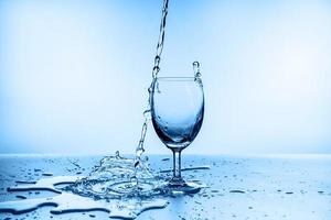 água espirrando de vidro isolado em fundo azul foto
