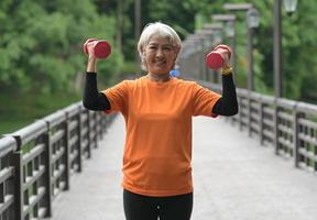 uma mulher asiática aposentada vestindo uma camiseta laranja está se exercitando ao ar livre, correndo, levantando halteres, esticando. foto