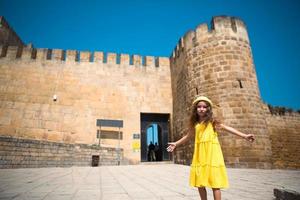 uma garota turista de chapéu amarelo e vestido de verão caminha pela rua da cidade velha feita de pedra com uma fortaleza. passeio turístico. a criança se perdeu, procurando os pais foto