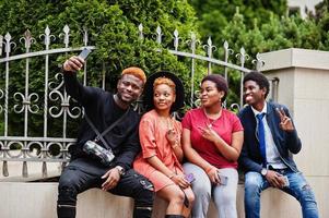 quatro amigos africanos se divertindo ao ar livre. duas garotas negras com caras com telefones celulares fazem selfie. foto