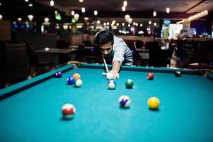 homem árabe elegante usa jeans jogando bilhar no bar. foto