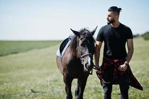 homem árabe de barba alta usa preto com cavalo árabe. foto