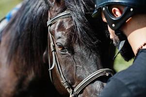 homem de barba alta árabe usar capacete preto com cavalo árabe. foto