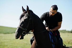 homem de barba alta árabe usar em cavalo árabe de passeio preto. foto