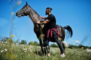 homem árabe de barba alta usa preto com cavalo árabe. foto