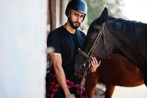 homem de barba alta árabe usar capacete preto com cavalo árabe. foto