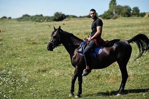 homem de barba alta árabe usar em cavalo árabe de passeio preto. foto