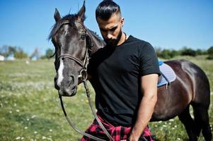 homem árabe de barba alta usa preto com cavalo árabe. foto