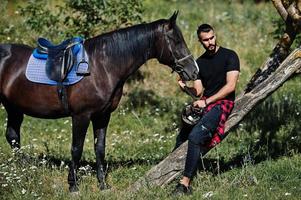 homem árabe de barba alta usa preto com cavalo árabe. foto