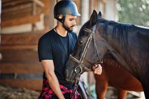 homem de barba alta árabe usar capacete preto com cavalo árabe. foto