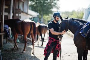 homem de barba alta árabe usar capacete preto com cavalo árabe. foto