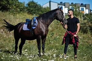 homem árabe de barba alta usa preto com cavalo árabe. foto