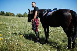 homem árabe de barba alta usa preto com cavalo árabe. foto