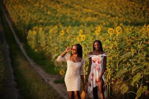 mulher de dois amigos negros muito jovens usam pose de vestido de verão em um campo de girassol. foto