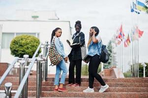 três estudantes africanos femininos posaram com mochilas e itens escolares no pátio da universidade e olhem para o livro. foto