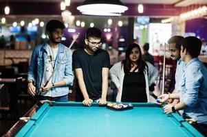 grupo de amigos asiáticos elegantes usam jeans jogando bilhar no bar. foto