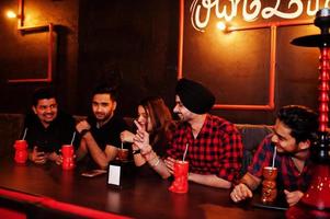 grupo de amigos indianos se divertindo e descansando na boate, bebendo coquetéis e fumando narguilé. foto