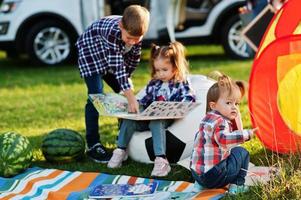 família passar tempo juntos. menina lendo livro ao ar livre com irmão e irmã. foto