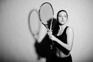 retrato preto e branco do jogador de mulher jovem e bonita em roupas esportivas, segurando a raquete de tênis em pé contra um fundo branco. foto