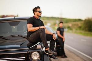 dois irmãos asiáticos vestem todo preto posando perto de carros suv. foto