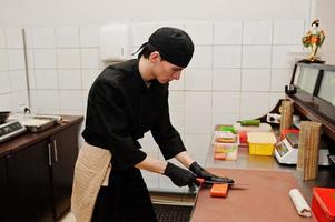 chef profissional veste de preto fazendo sushi e pãezinhos em uma cozinha de restaurante de comida tradicional japonesa. foto