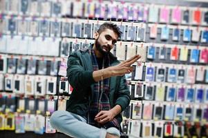 comprador de cliente de homem de barba indiana na jaqueta na loja de telefones celulares. conceito de povos e tecnologias do sul da Ásia. loja de celulares. foto