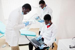 três médicos afro-americanos trabalhando com laptop, discutindo com colegas na clínica odontológica. foto
