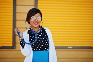 médico americano africano fêmea com estetoscópio posou obturador amarelo de fundo ao ar livre.