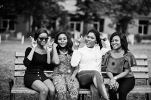 grupo de quatro garotas afro-americanas sentadas no banco ao ar livre e colocar as mãos no ar. foto