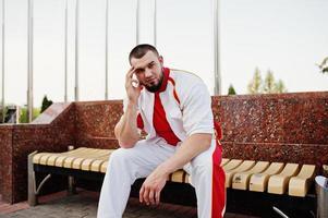 jovem homem musculoso barbudo brutal usar terno branco esporte com camisa vermelha. foto
