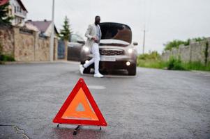 triângulo de aviso vermelho de emergência no carro suv quebrado do sinal de estrada do homem africano. foto