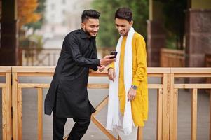 dois amigos indianos elegantes em roupas tradicionais posaram ao ar livre e olhando no celular. foto