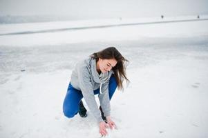 garota engraçada usar suéter com capuz e jeans, no lago congelado em dia de inverno. foto