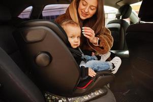 jovem mãe e filho no carro. assento de bebê na cadeira. conceito de condução de segurança. foto