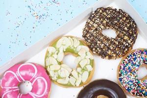 rosquinhas sortidas com cobertura de chocolate, cobertura polvilha rosquinhas variedade colorida e variedade de sabores mistura de rosquinhas doces multicoloridas com fosco polvilhado sobre fundo azul. vista do topo foto