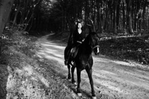 garota mística em grinalda veste de preto a cavalo em madeira. foto